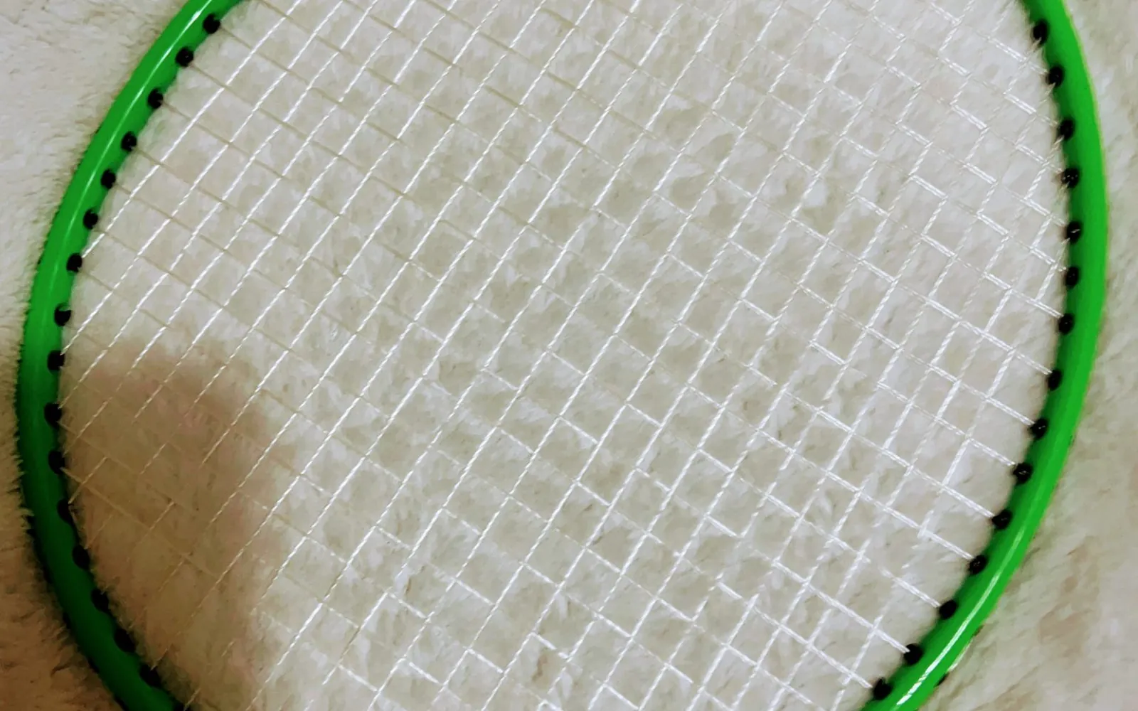 Close-up of a green badminton racket head with white strings