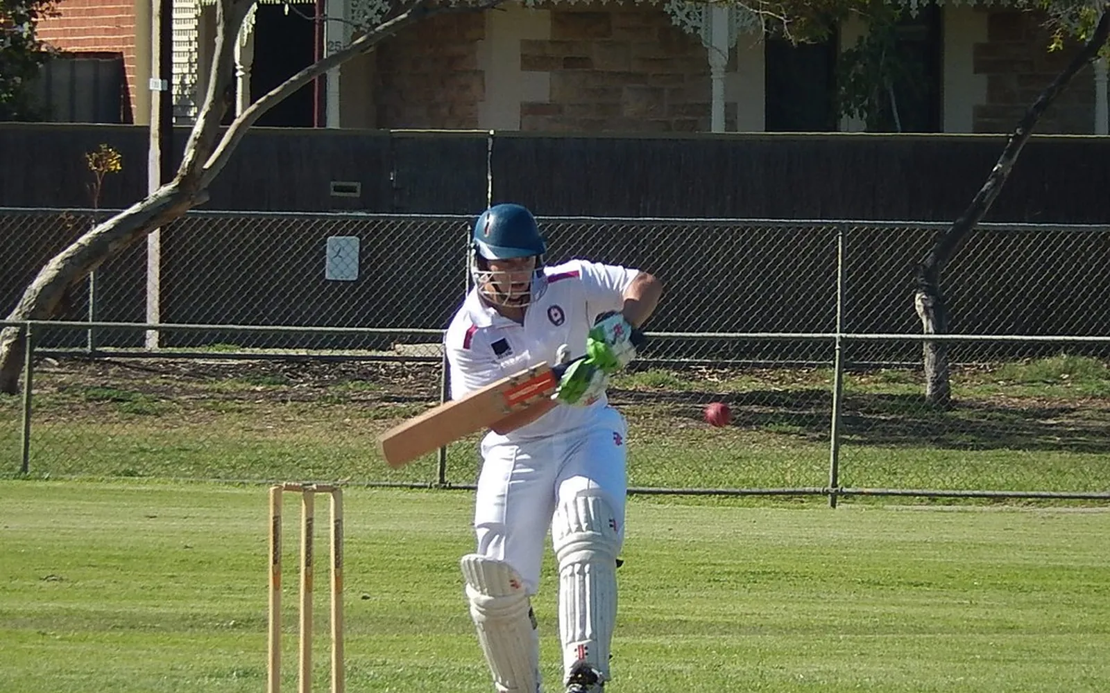 A batter in helmet, pads and gloves playing a shot during a club cricket match