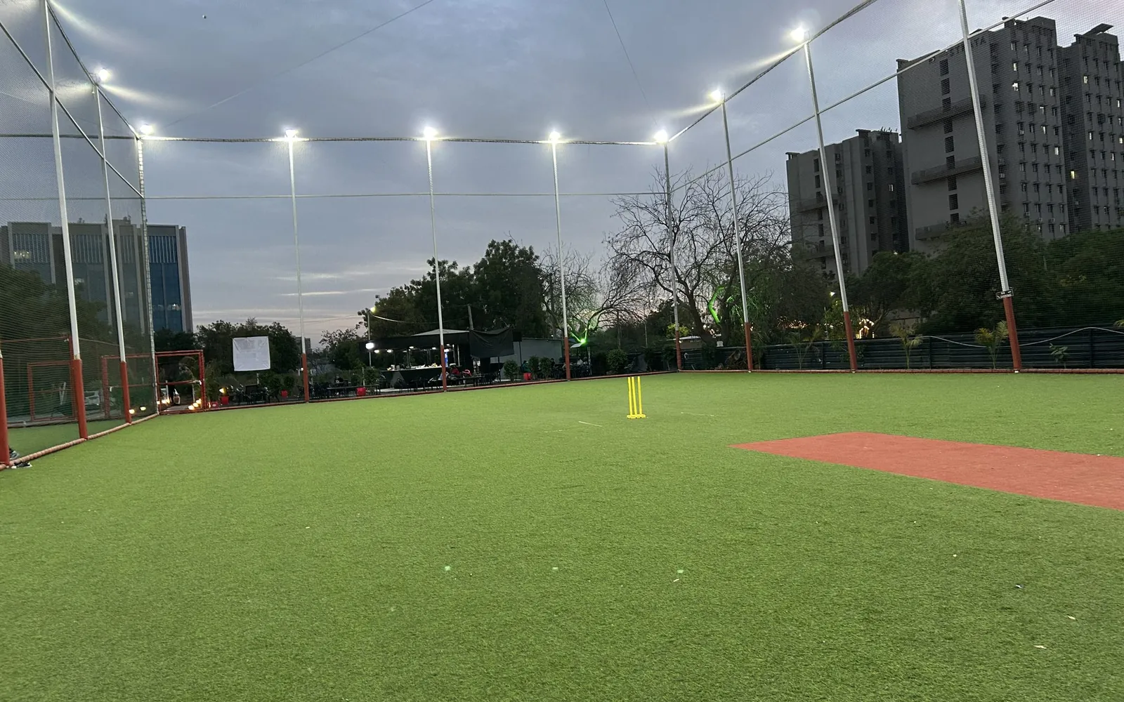An artificial-turf sports ground enclosed by nets under floodlights at dusk
