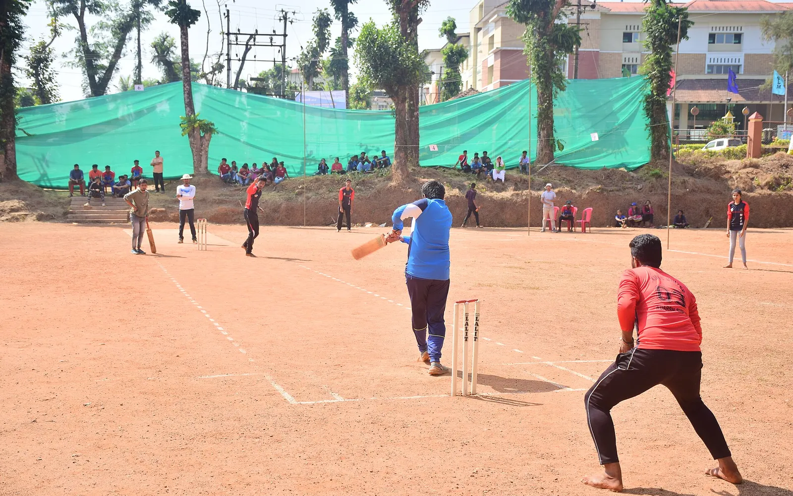 A young batter and wicketkeeper during a cricket match on an earth ground