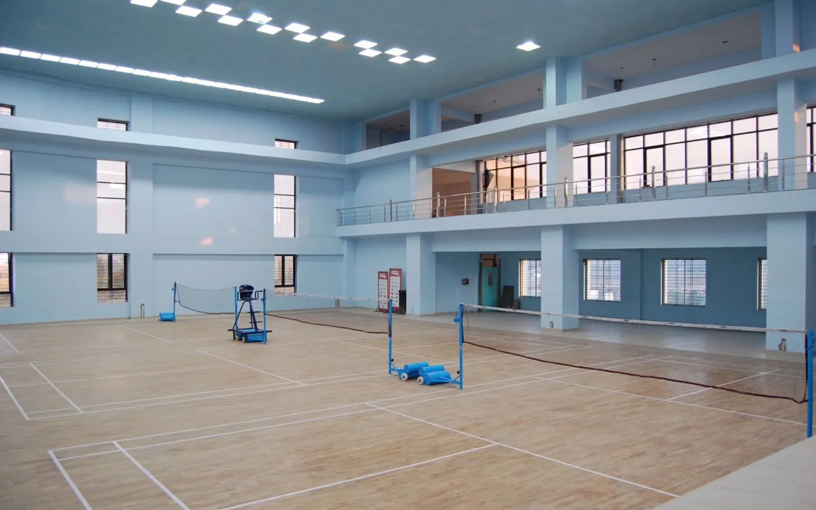 An indoor sports hall with a wooden floor set up for badminton coaching