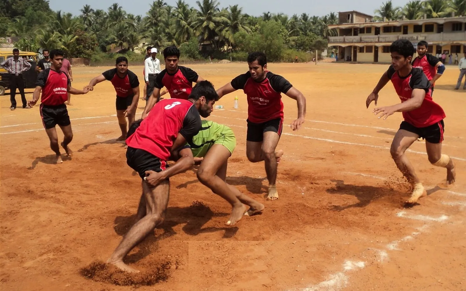 A raider being tackled by defenders during a kabaddi match on a mud court