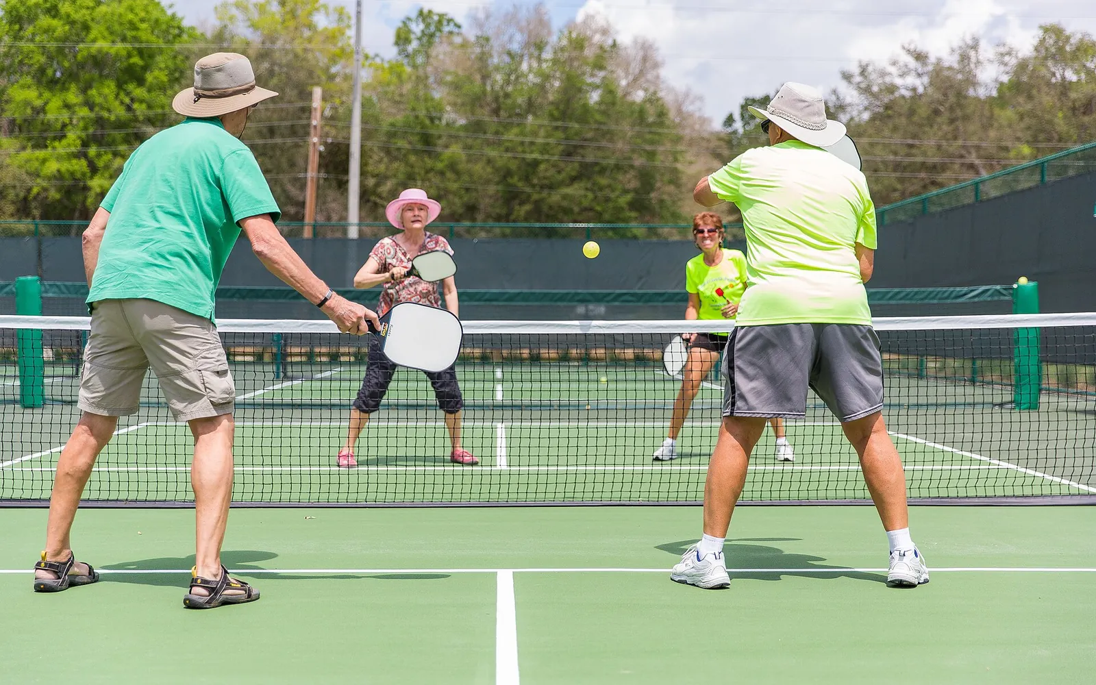 Four players in a doubles pickleball game at the net on an outdoor court