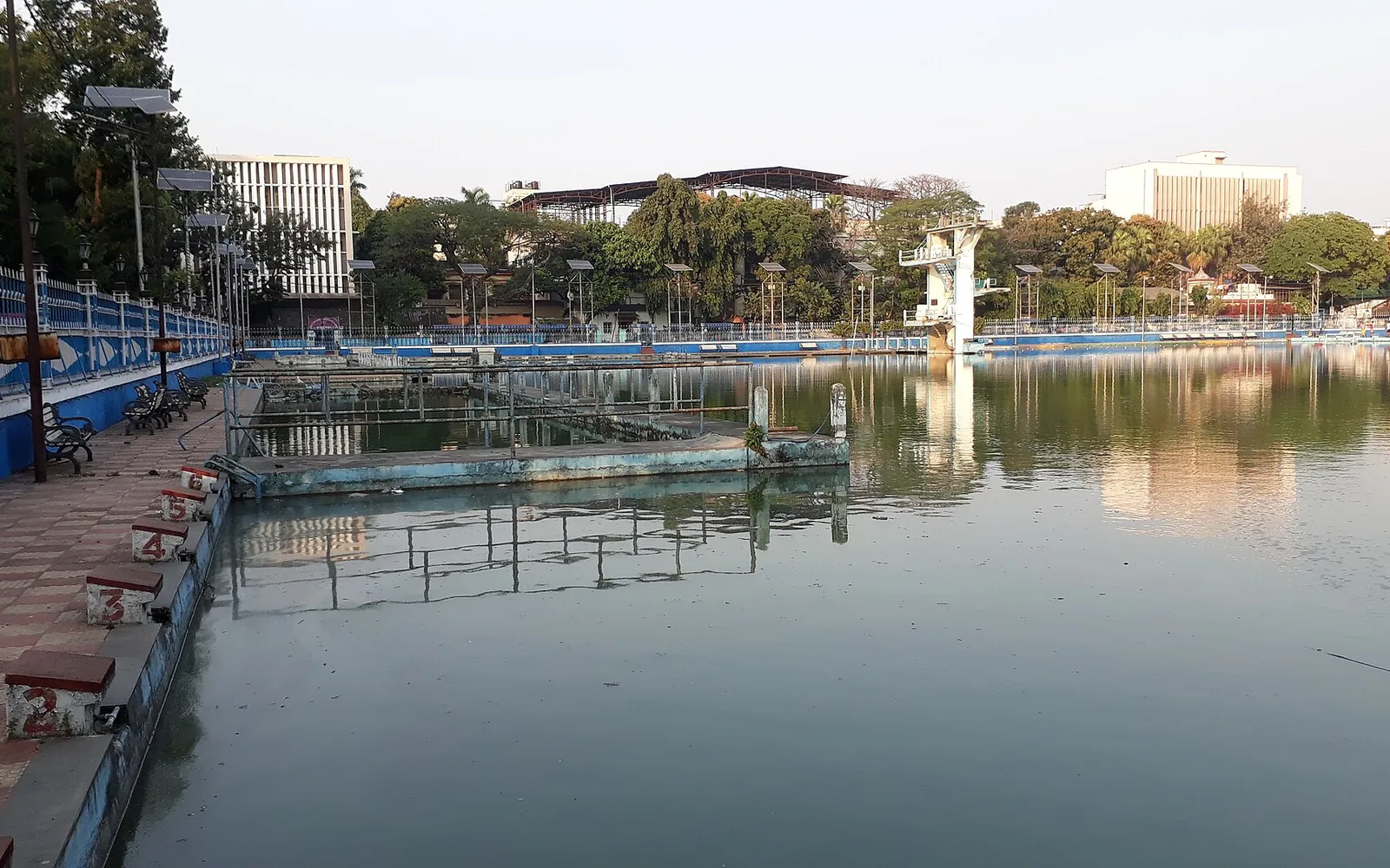 A large outdoor public swimming pool in an Indian city with diving tower and spectator steps
