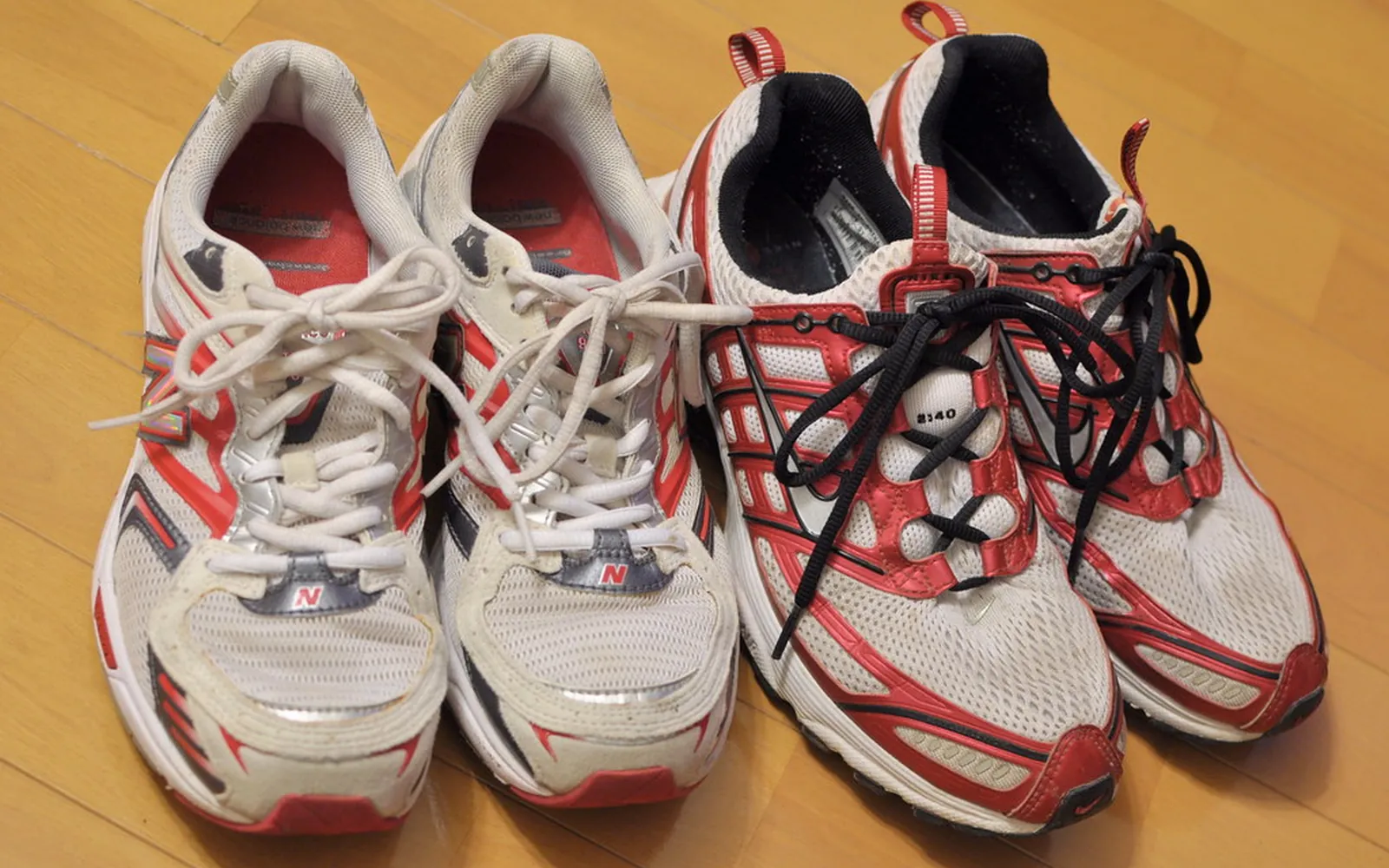 Two pairs of well-worn running shoes side by side on a wooden floor