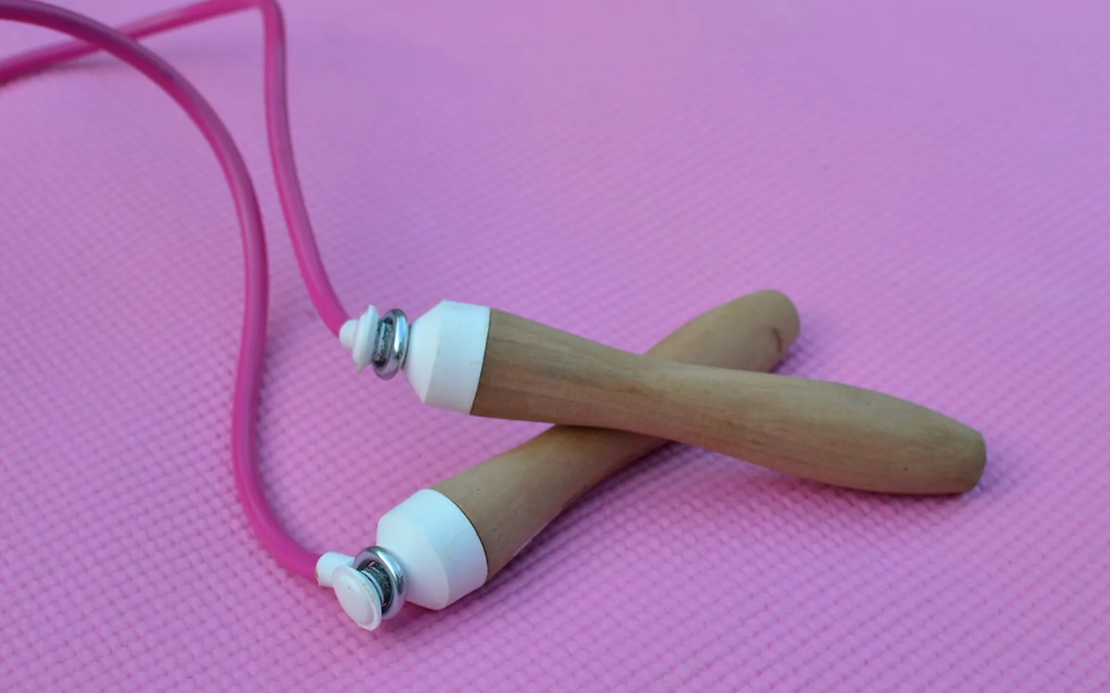 A skipping rope with wooden handles lying on a pink exercise mat