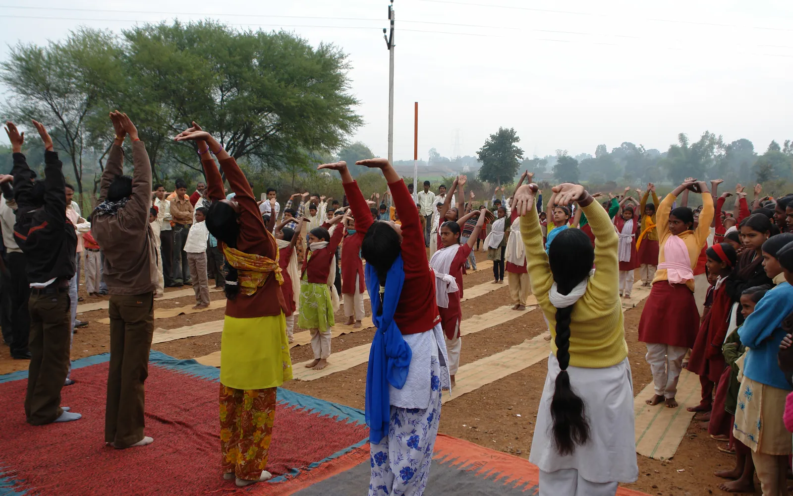 Students and teachers doing Surya Namaskar together on mats outdoors in India