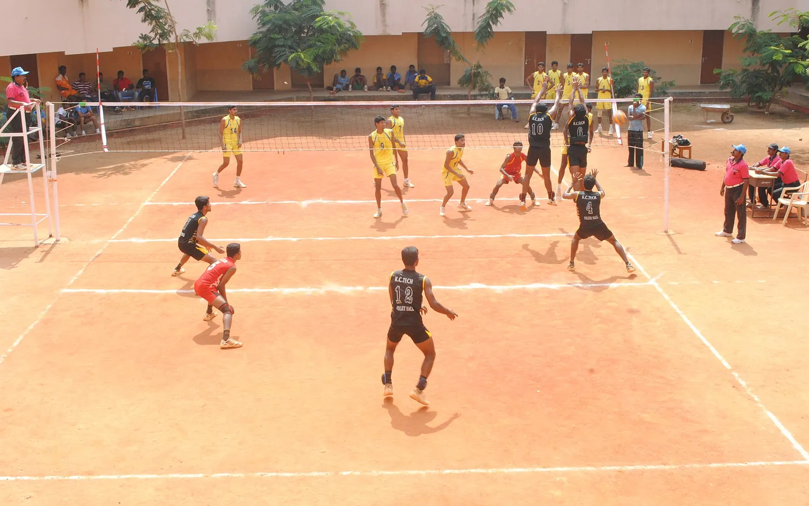 Players competing in an outdoor volleyball tournament watched by spectators